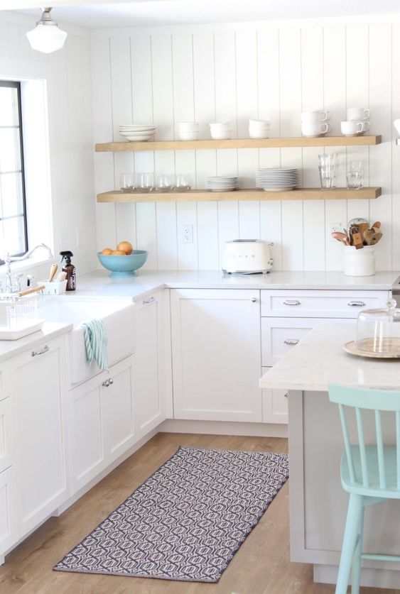 a small white Scandinavian kitchen with shaker cabinets, a white beadboard backsplash, stained shelves and a printed rug