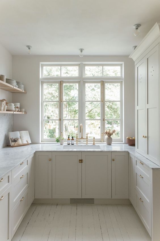 a small yet cool white kitchen with shaker cabinets, white stone countertops, open shelves, gold fixtures