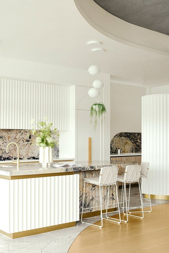 a sophisticated white kitchen with ribbed cabinets and a kitchen island, a bold stone backsplash and countertops