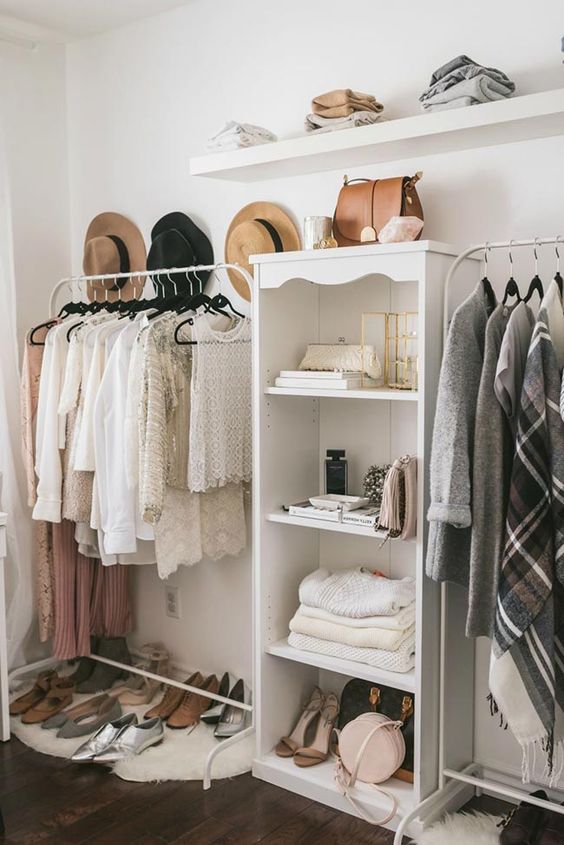 a stylish and cute makeshift closet with white metal racks, a white storage shelf, an open shelf and a hat display