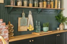 a stylish black kitchen with shaker cabinets, a dark green beadboard backsplash and stained shelves plus butcherblock countertops