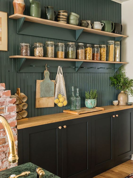 a stylish black kitchen with shaker cabinets, a dark green beadboard backsplash and stained shelves plus butcherblock countertops