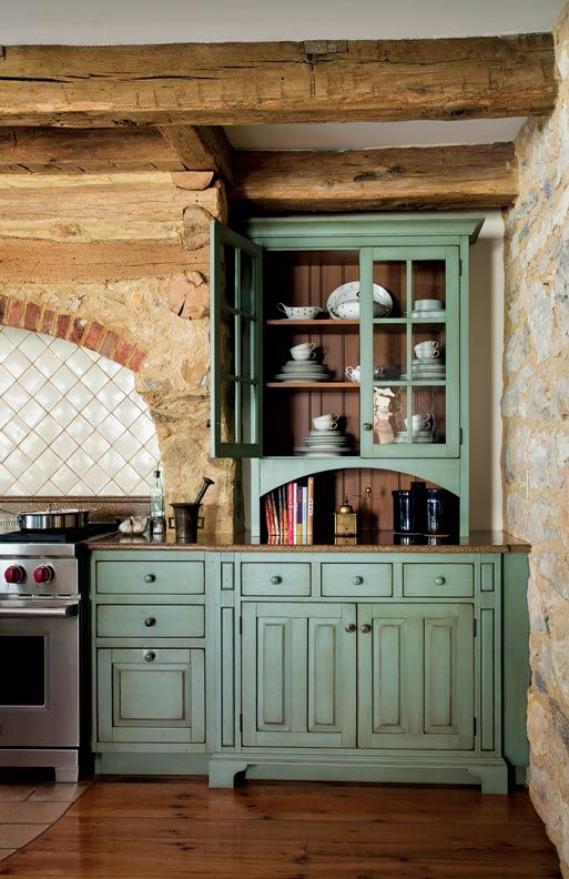 a stylish kitchen with stone walls, green cabinets, rough wooden beams that adds to the rustic coziness of the space