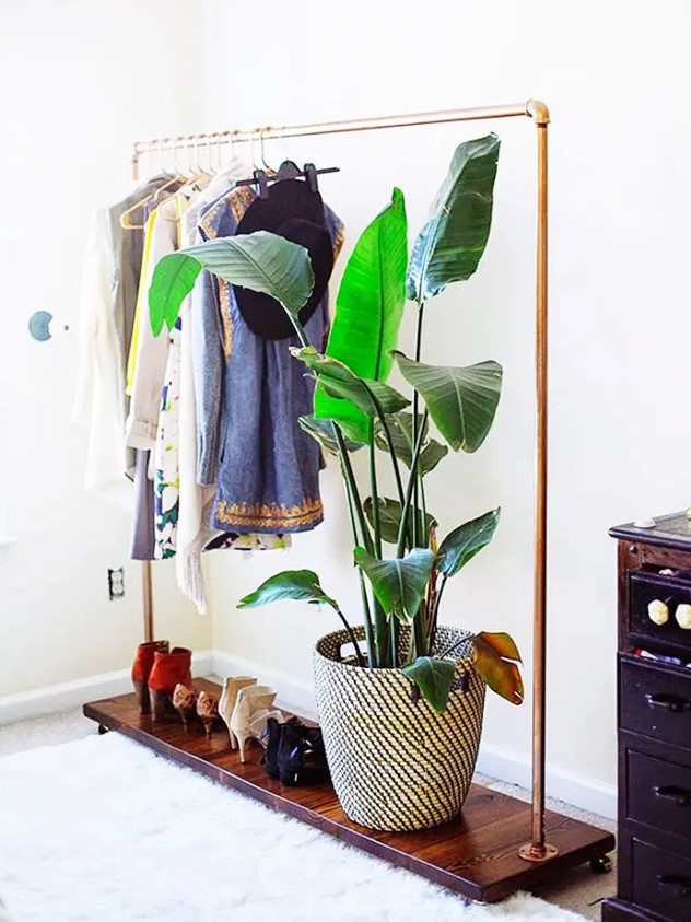 a stylish makeshift closet with a metal and stained wood rack for clothes and shoes and a dark stained dresser plus a potted plant