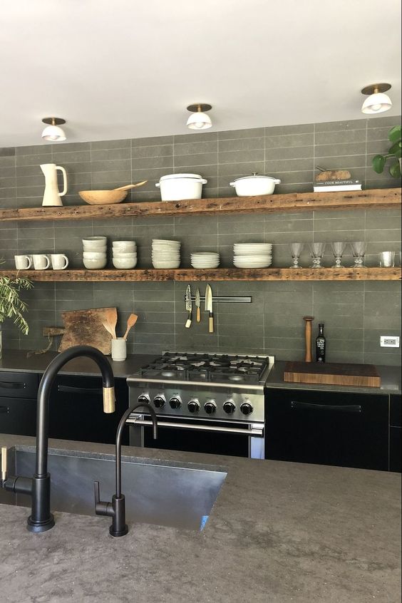 a stylish modern kitchen with black cabinets, concrete countertops, rough wood shelves and potted greenery