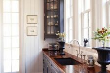 a vintage cottage kitchen with white beadboard walls, navy cabinets and a butcherblock countertop, a printed rug