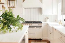 a vintage creamy kitchen with shaker and usual cabinets, a large kitchen island, a creamy beadboard backsplash and vintage lanterns