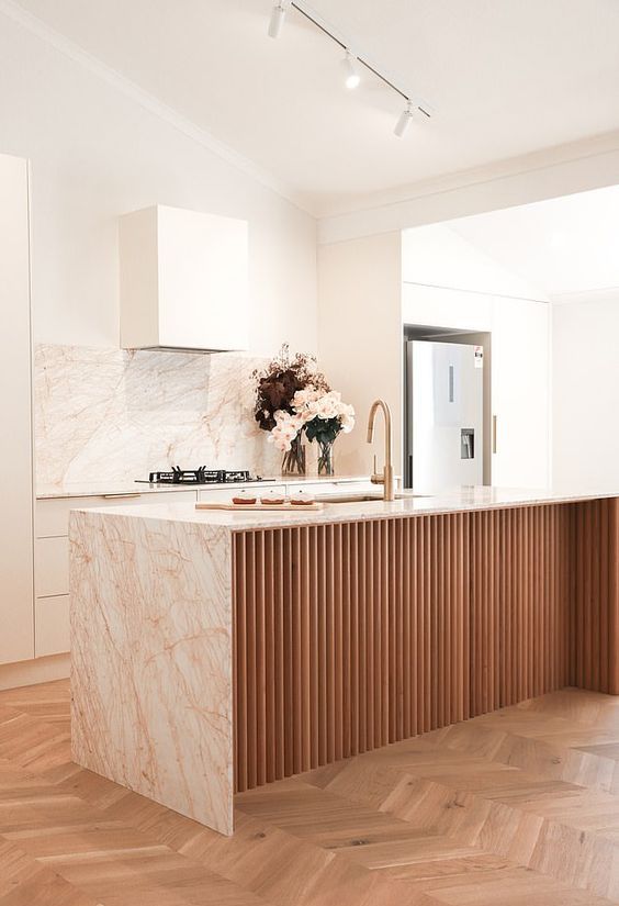 a warm neutral kitchen with white cabinets, a fluted kitchen island, pink marble countertops and a backsplash