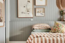 a welcoming bedroom with green beadboard walls, a bed with printed bedding, a small gallery wall and woven lamps