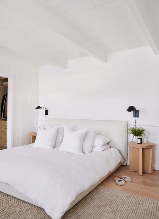 a welcoming white bedroom with a white bed, wooden bedside tables, black sconces and a soft rug