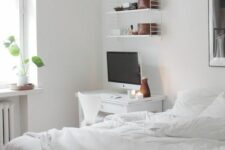 a white Nordic bedroom with a bed and white bedding, a white desk and a shelf, a potted plant