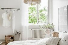 a white Scandinavian bedroom with a bed with neutral bedding, a makeshift closet, a basket, a woven pendant lamp