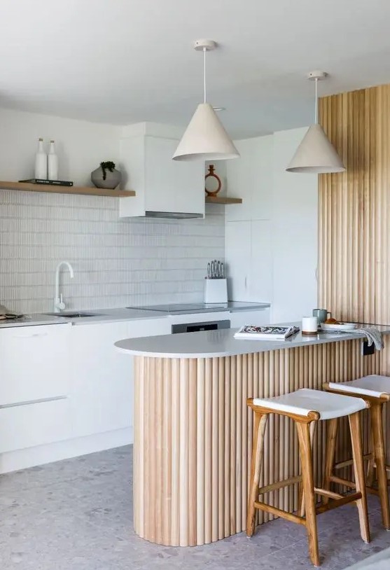 a white Scandinavian kitchen with grey stone countertops, open shelves, a fluted kitchen island and lamps over it