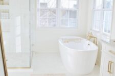 a white bathroom with large windows, a shower space enclosed in glass, an oval tub, a printed rug and gold fixtures
