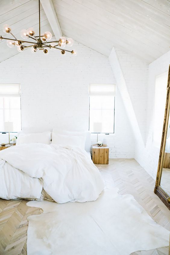 a white bedroom with a bed and white bedding, tree stumps as nightstands with white lamps and a chandelier