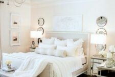 a white bedroom with a contrasting floor, an upholstered bed with white bedding, mirror nightstands and a bench
