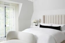 a white bedroom with a creamy upholstered bed, neutral bedding, a creamy daybed, a chandelier of bubbles