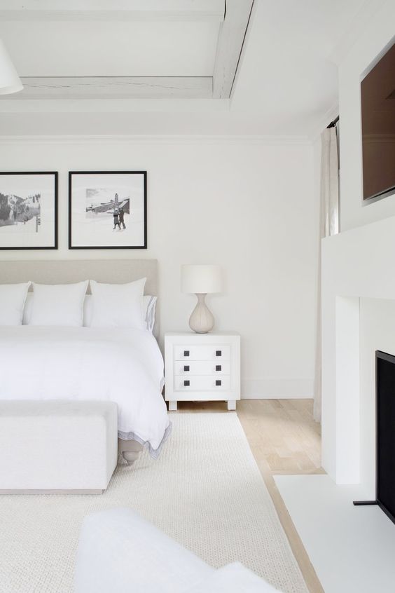 a white bedroom with an upholstered bed and white bedding, an upholstered bench, a white nightstand and a gallery wall
