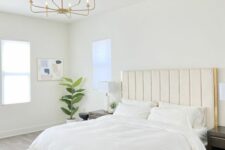 a white bedroom with an upholstered bed, white bedding, dark nightstands, potted greenery and a chic gold chandelier