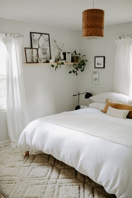 a white boho bedroom with a wooden bed, nightstands, black lamps and a woven one, a shelf with books and greenery