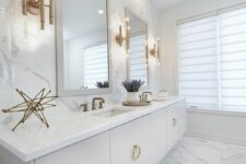 a white contemporary bathroom with a floating vanity, white marble tiles and brass and gold fixtures and decor for more elegance