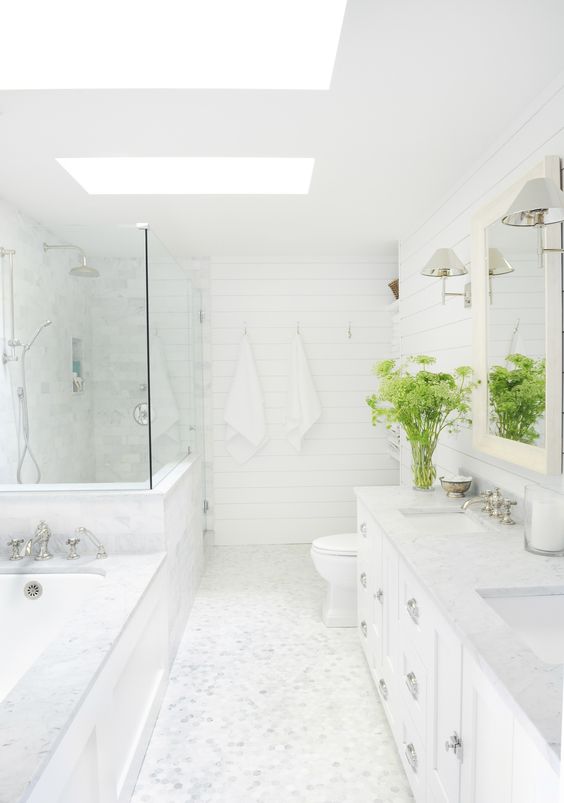 a white farmhouse bathroom with skylights, a shower space and a tub, a mirror in a frame, a large vanity and greenery
