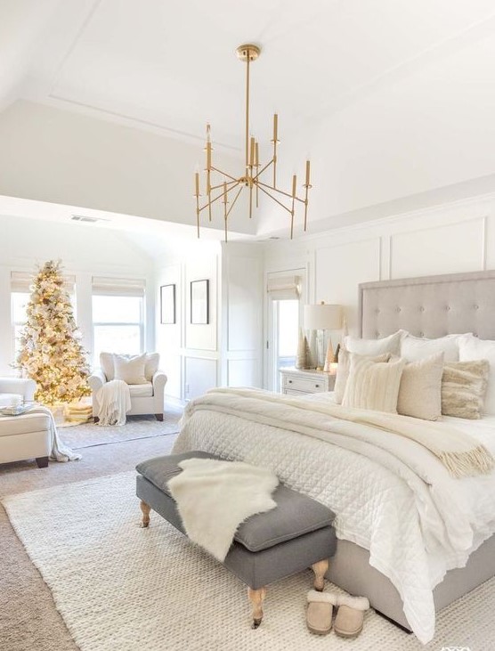 a white farmhouse bedroom with a grey bed, a grpahite grey bench, white chairs and gold touches