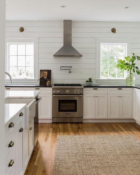 a white farmhouse kitchen with shaker cabinets, a white shiplap backsplash, black and white countertops