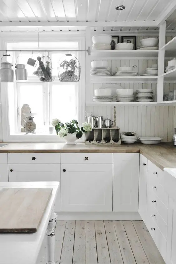 a white farmhouse kitchen with shaker cabinets, open shelves, butcherblock countertops and a tan beadboard backsplash