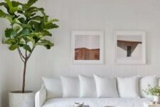 a white farmhouse living room with a white sofa, a printed rug, a wooden coffee table, a potted plant and a gallery wall