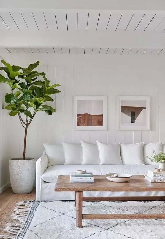 a white farmhouse living room with a white sofa, a printed rug, a wooden coffee table, a potted plant and a gallery wall