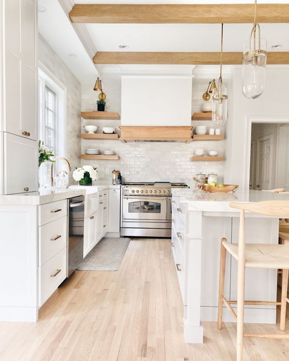 a white kitchen with a white subway tile backsplash, a large kitchen island, wooden beams and wooden shelves
