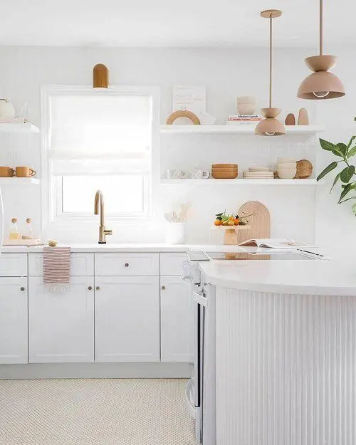 a white kitchen with shaker style and fluted cabinets, white stone countertops and brass touches