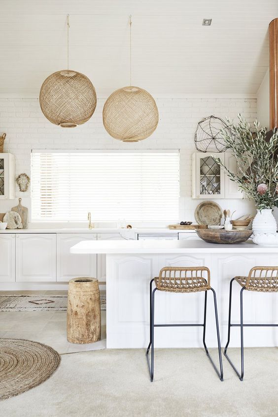 a white kitchen with vintage inspired cabinets, tall woven stools and a wooden vase, woven pendant lamps
