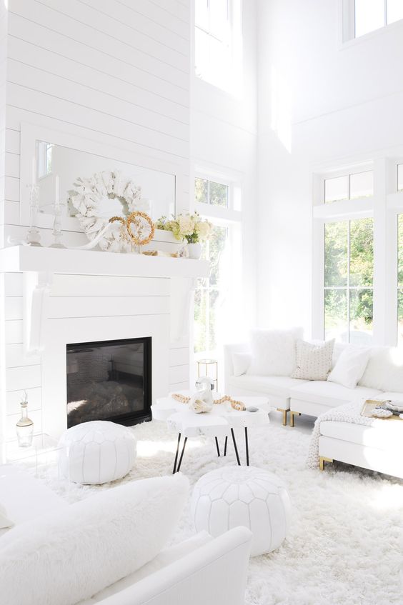 a white living room with a double-height ceiling, a built-in fireplace with a slatted wall, white seating furniture and coastal decor