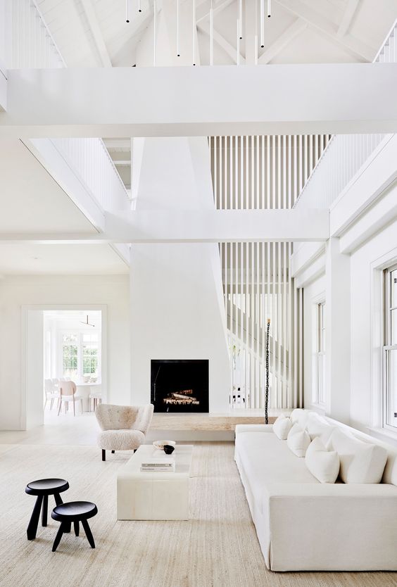 a white living room with a fireplace, a sofa, a table, chair, black side tables and a chandelier is a chic and refined space
