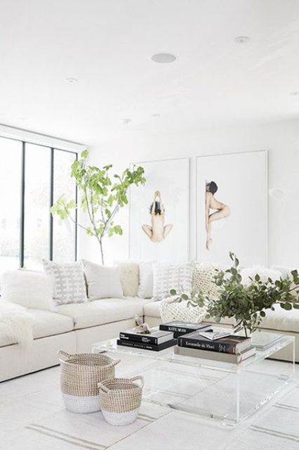 a white living room with a large corner sofa, lots of pillows, acrylic tables, greenery and artwork feels soothing