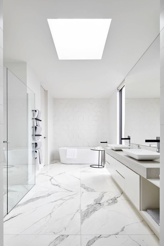 a white minimalist bathroom with catchy tiles of various sizes, a skylight, a large mirror and vanity, a tub and a shower space