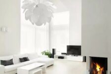 a white minimalist living room with simple and comfy furniture, a built-in fireplace, a petal lamp and much natural light