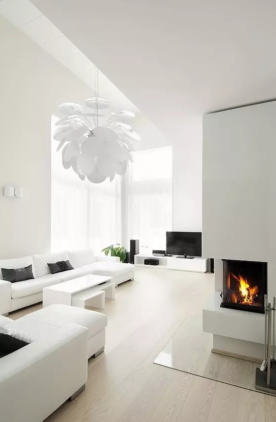 a white minimalist living room with simple and comfy furniture, a built in fireplace, a petal lamp and much natural light