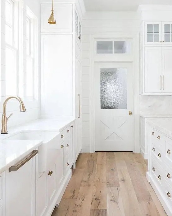 a white vintage farmhouse kitchen with brass handles and wooden floors that make it cozier