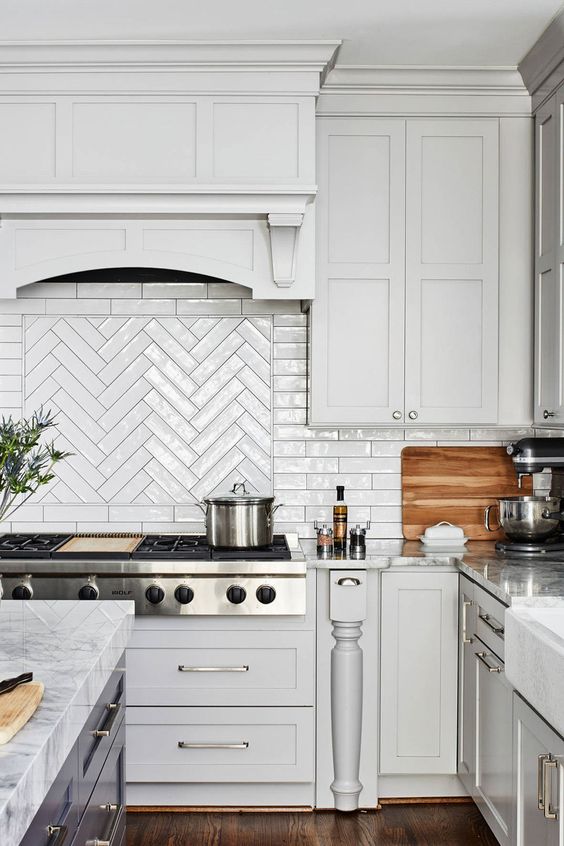 a white vintage farmhouse kitchen with shaker cabinets, a herringbone tile backsplash and a dark kitchen island