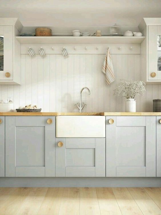 an airy kitchen with light grey shaker cabinets, a white beadboard backsplash, butcherblock countertops and an open shelf
