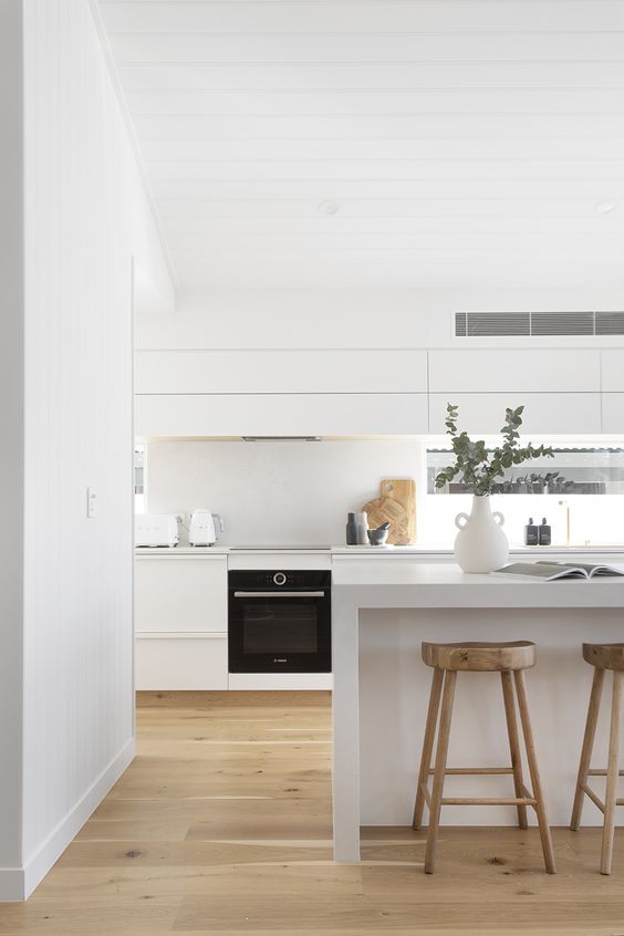 an airy white kitchen with sleek cabinets, a large kitchen island, a window backsplash and stained stools