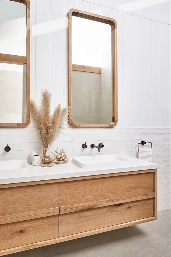 an all-white bathroom clad with tiles and beadboard and spruce up with a floating timber vanity, mirrors in wooden frames
