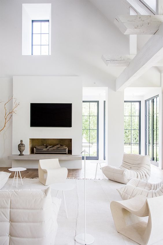 an all white living room with a fireplace, neutral furniture, chairs and side tables and lots of light coming in