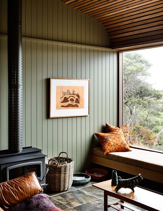 an attic living room with green beadboard on the walls, an upholstered bench, bright pillows, a hearth and a basket
