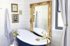 an eclectic bathroom clad with white beadboard, with a navy tub, a statement mirror, a crystal chandelier and a gallery wall