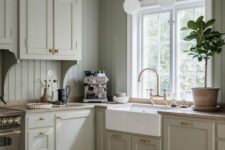 an elegant greige kitchen with shaker cabinets, a matching beadboard backsplash, butcherblock countertops and brass fixtures