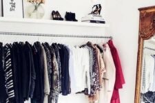 an elegant makeshift closet with a long railing for hanging clothes, an open shelf for shoes and other stuff and a mirror in a heavy frame